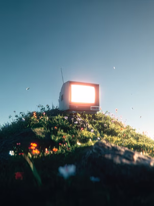 Vintage television glowing brightly atop a grassy hill with wildflowers under a clear blue sky.